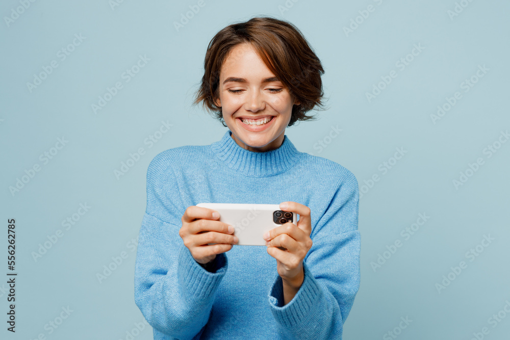 Gambling young happy woman wear knitted sweater use play racing app on mobile cell phone hold gadget smartphone for pc video games isolated on plain pastel light blue cyan background studio portrait. Gambling young happy woman wear knitted sweater use play racing app on mobile cell phone hold gadget smartphone for pc video games isolated on plain pastel light blue cyan background studio portrait.