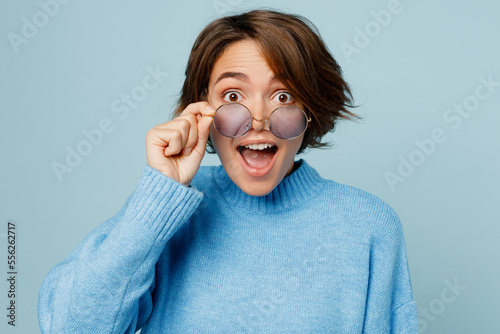 Quadro su tela Young surprised shocked happy cheerful caucasian woman wearing knitted sweater lower glasses look camera isolated on plain pastel light blue cyan background studio portrait