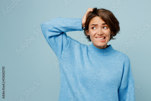 Young sad caucasian woman wearing knitted sweater look aide on workspace area mock up scratch hold head say oops isolated on plain pastel light blue cyan background studio. People lifestyle concept.
