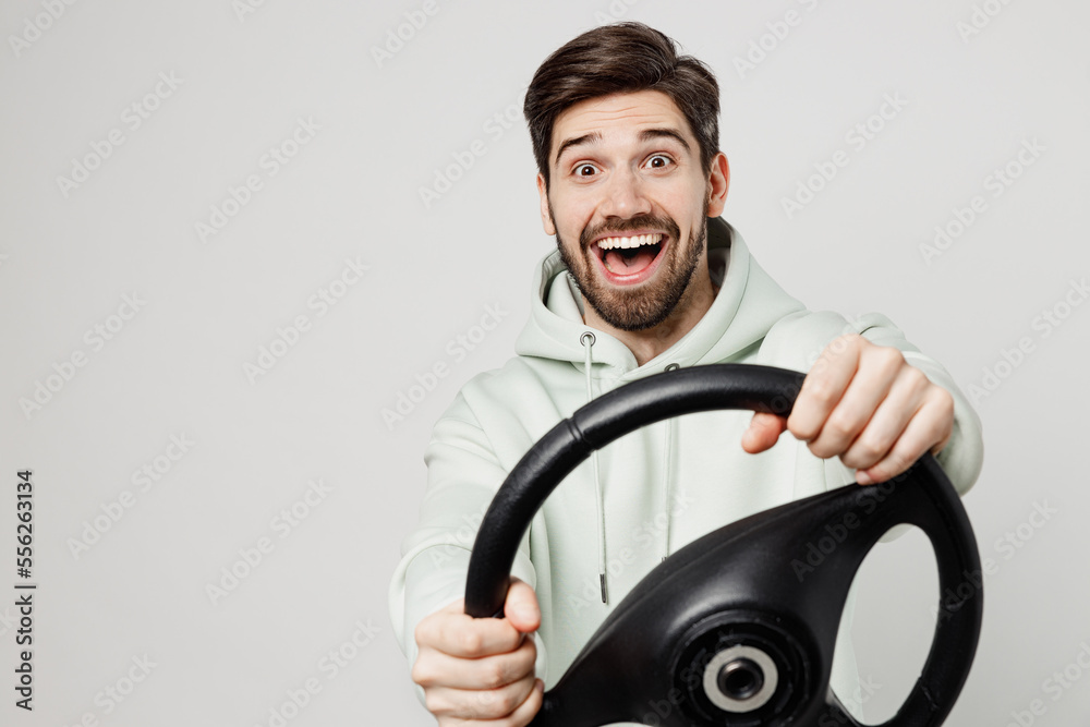 Young surprised happy fun satisfied amazed caucasian man wear mint hoody look camera hold steering wheel driving car isolated on plain solid white background studio portrait. People lifestyle concept. Young surprised happy fun satisfied amazed caucasian man wear mint hoody look camera hold steering wheel driving car isolated on plain solid white background studio portrait. People lifestyle concept.