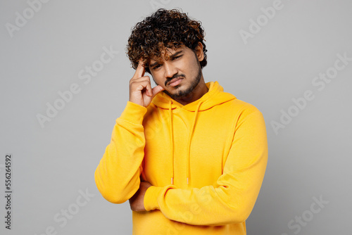 Young minded worried toughtful concerned Indian man 20s he wearing casual yellow hoody looking camera prop up chin think isolated on plain grey background studio portrait. People lifestyle portrait. photo