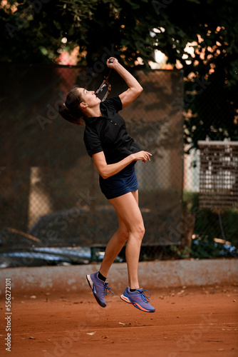 side view of active bouncing woman tennis player with tennis racket in hand doing pitch
