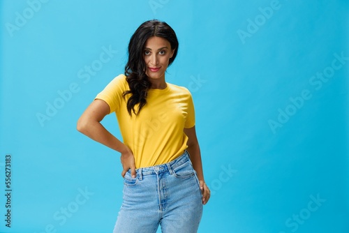 Woman in yellow t-shirt on blue background posing gestures emotions and signals with smile, hands up happiness copy space