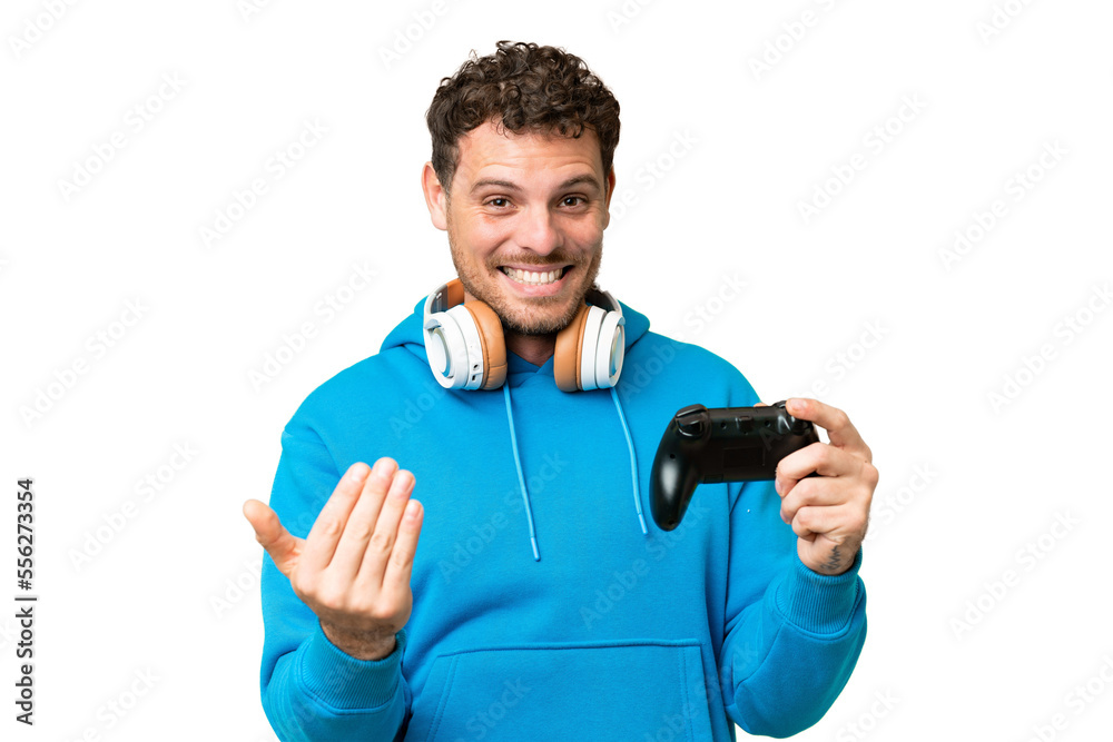 Brazilian man playing with a video game controller over isolated chroma key background inviting to come with hand. Happy that you came Brazilian man playing with a video game controller over isolated chroma key background inviting to come with hand. Happy that you came