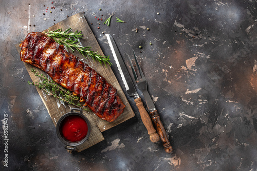hot grilled spare ribs on cutting board on a dark background. American Spare Ribs in BBQ Sauce. Restaurant menu, dieting, cookbook recipe top view