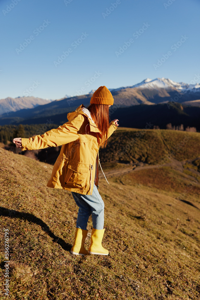 Woman's back full-length jogging walks on the hill and looking at the mountains in a yellow raincoat and jeans in the autumn happy sunset trip on a hike, freedom lifestyle Woman's back full-length jogging walks on the hill and looking at the mountains in a yellow raincoat and jeans in the autumn happy sunset trip on a hike, freedom lifestyle