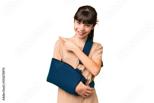 Little caucasian girl with broken arm and wearing a sling over isolated background pointing to the side to present a product