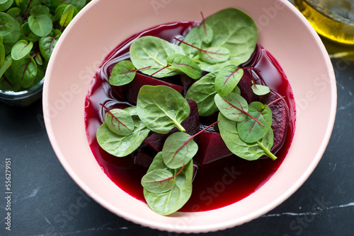 Middle close-up of beetroot soup served in a roseate bowl with fresh spinach and beetroot leaves, elevated view