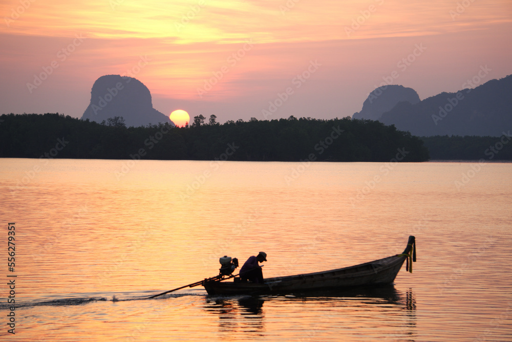 Silhouette of asian fisherman is driving a wooden boat in the sea with sunrise morning background at Ban Sam Chong Tai, Ta Kua Thung, Phangnga, Thailand.