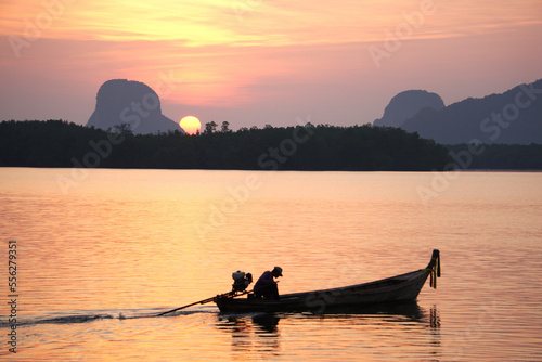 Silhouette of asian fisherman is driving a wooden boat in the sea with sunrise morning background at Ban Sam Chong Tai, Ta Kua Thung, Phangnga, Thailand.