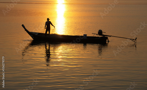Silhouette of asian fisherman on a wooden boat preparing a net for catching freshwater fish in the early morning, Ban Sam Chong Tai, Ta Kua Thung, Phangnga, Thailand.