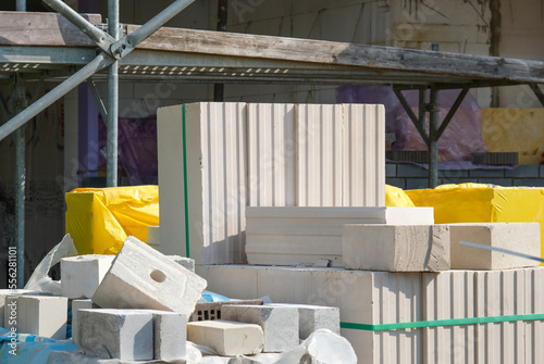 Stapel unterschiedlicher Steine für den Hausbau auf einer Baustelle, Gerüst und Teile des Neubaus im Hintergrund, selektiver Fokus .. photo