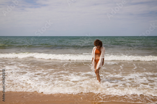 Young beautiful woman in bikini walking along the beach shore. The woman is enjoying her trip to a paradise beach while making different gestures and expressions. Holidays and travels.