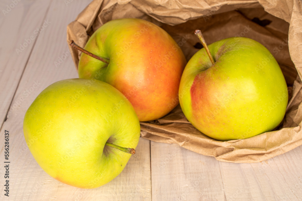 Three sweet green apples with a paper bag on a wooden table, macro.