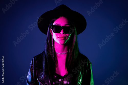 Stylish rock woman in neon multi-color light. Smoky background, night party, disco club. Z generation enigmatic pretty lady in hat, eyewear