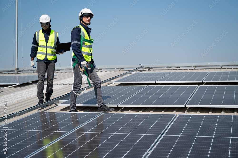 Caucasian and African American engineer man holding electric screwdriver and computer notebook walk and checking solar panel on roof factory Caucasian and African American engineer man holding electric screwdriver and computer notebook walk and checking solar panel on roof factory