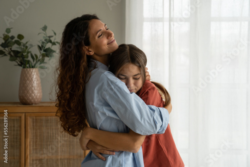 Young loving mother hugging her teenage daughter, mom demonstrating unconditional love for child, mommy cuddling supporting upset teen girl while spending time together at home Fototapet