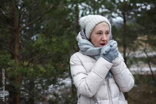 Portrait of beautiful happy senior retired elderly woman is freezing walking outdoors in winter snowy park or forest, wood, at cold frosty day in hat, scarf, gloves, in snow, trembles