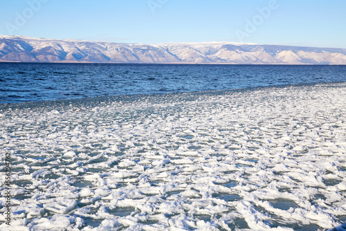 The beginning of the freezing of Lake Baikal on a sunny December day. Winter landscape. Snow and ice floes near the shore, open water in the lake.