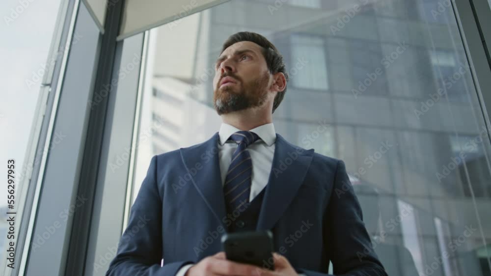Stressed businessman ending phone call standing near office window closeup. Stressed businessman ending phone call standing near office window closeup.