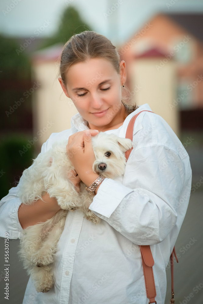 Portrait of a young beautiful fair-haired girl on a summer day outdoors, with a lap dog in her arms. Portrait of a young beautiful fair-haired girl on a summer day outdoors, with a lap dog in her arms.