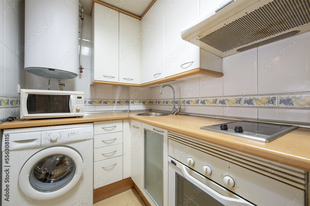 Corner of a kitchen with white furniture with drawers and cabinets, electric hot water heater and white appliances Corner of a kitchen with white furniture with drawers and cabinets, electric hot water heater and white appliances
