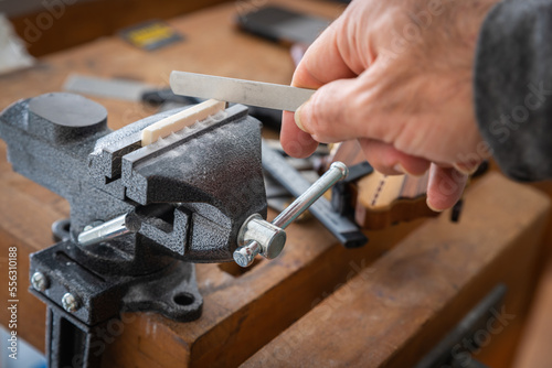 Worker's hand repairs guitar bone nut and slotting
