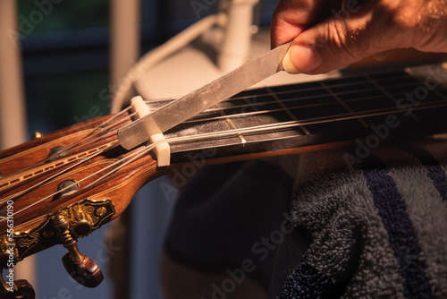 Worker's hand repairs guitar bone nut on classical guitar and slotting