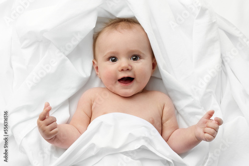 Funny baby lying in bed with surprised expression