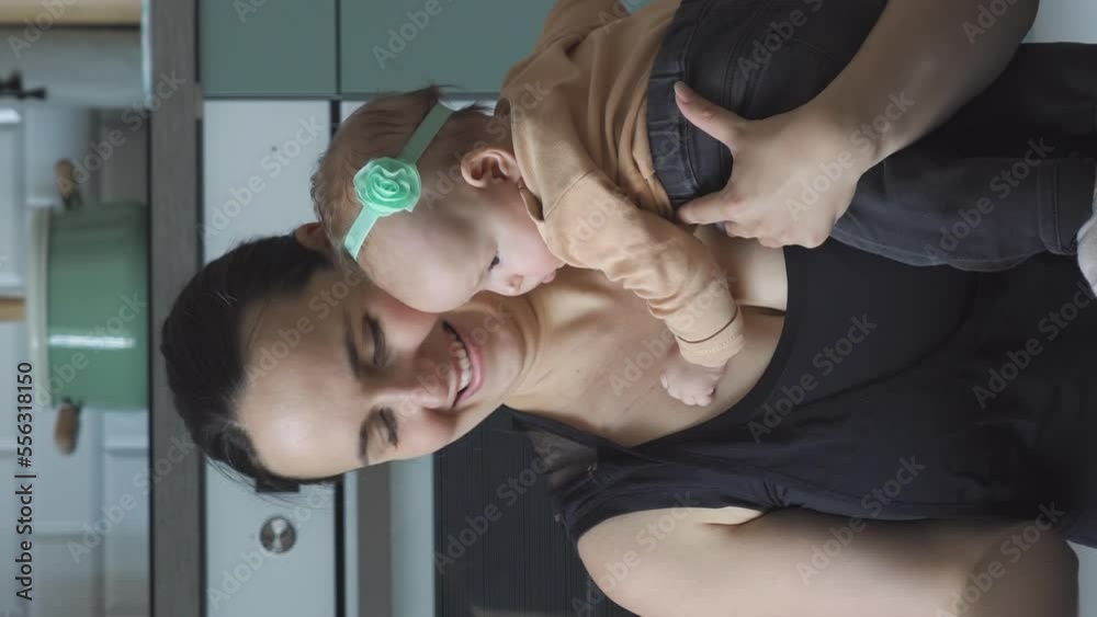 Vertical video. Happy young mother holding baby in hands while training with dumbbells in the kitchen