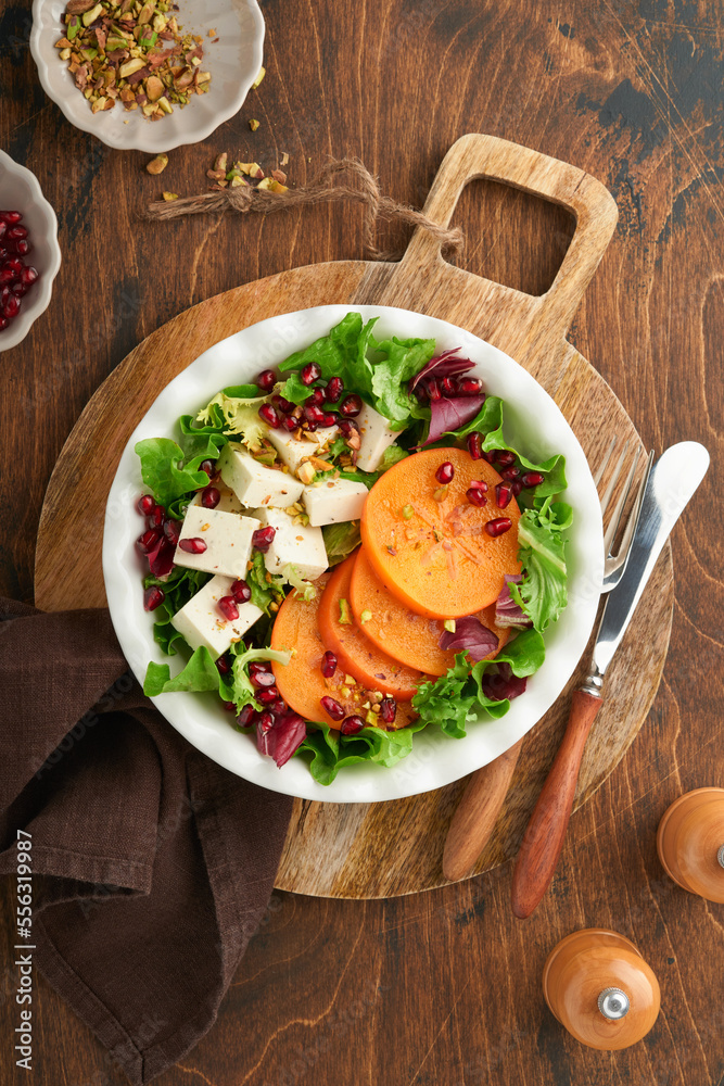 Salad. Fresh green salad with feta cheese, persimmon, pomegranate and pistachio on white plate. Idea for healthy delicious winter Christmas salad. Healthy balanced eating. Top view. Salad. Fresh green salad with feta cheese, persimmon, pomegranate and pistachio on white plate. Idea for healthy delicious winter Christmas salad. Healthy balanced eating. Top view.