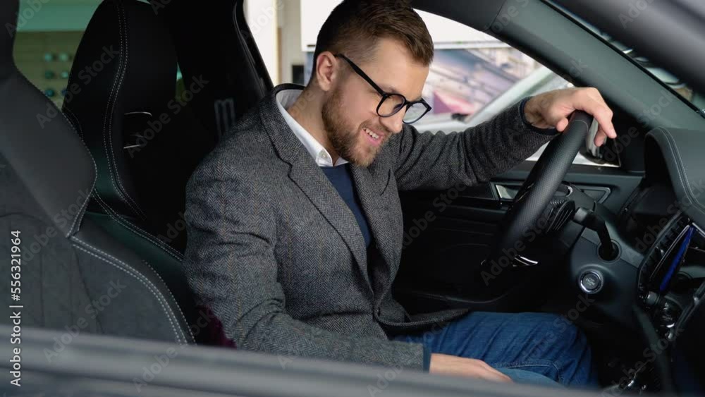 Happy man sits in new electric car in shop dealership and celebrate purchase of new vehicle. Buy car Happy man sits in new electric car in shop dealership and celebrate purchase of new vehicle. Buy car