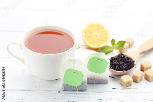 Cup of tea with tea bags, sugar cubes and lemon on white wooden table