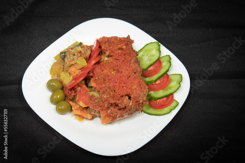 Potatoes and meat with vegetables in tomato sauce on a white plate