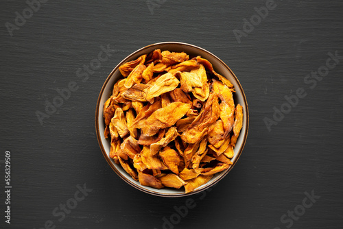 Delicious Organic Dried Mango Fruit in a Bowl on a black background, top view. Flat lay, overhead, from above.