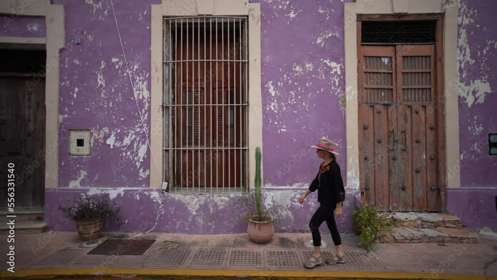 Pretty, mature, woman walking on a sidewalk along colorful buildings in Merida, Yucatan, Mexico. Pretty, mature, woman walking on a sidewalk along colorful buildings in Merida, Yucatan, Mexico.
