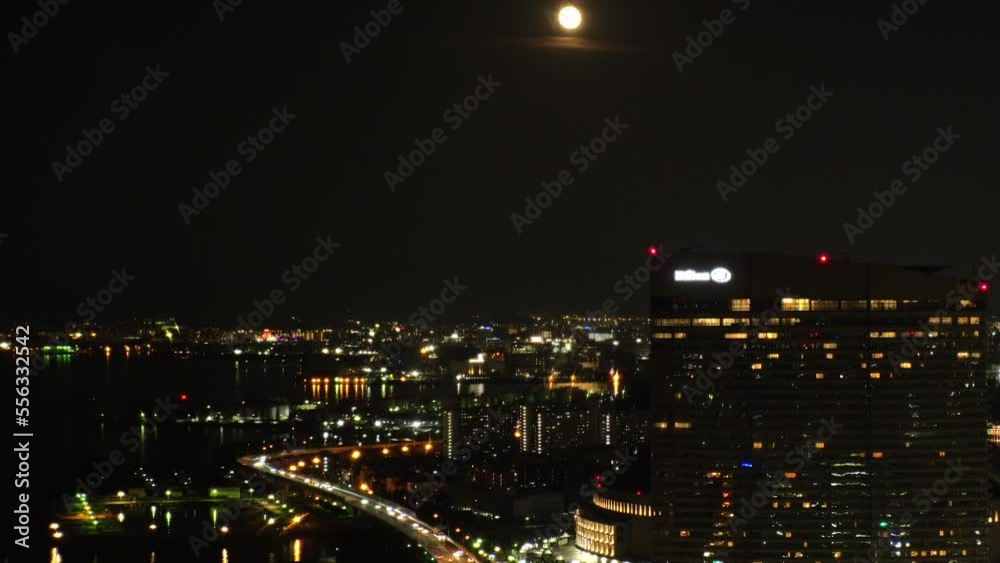 FUKUOKA, JAPAN - NOV 2022 : Aerial high angle view of Fukuoka City and full moon. Time lapse shot at night. View around Tenjin and Nakasu downtown area. Travel and urban city nightlife concept video.