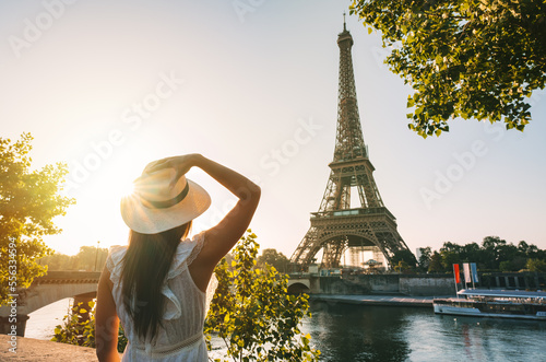 Young woman tourist in sun hat and white dress standing in front of Eiffel Tower in Paris at sunset. Travel in France, tourism concept © Creative Cat Studio