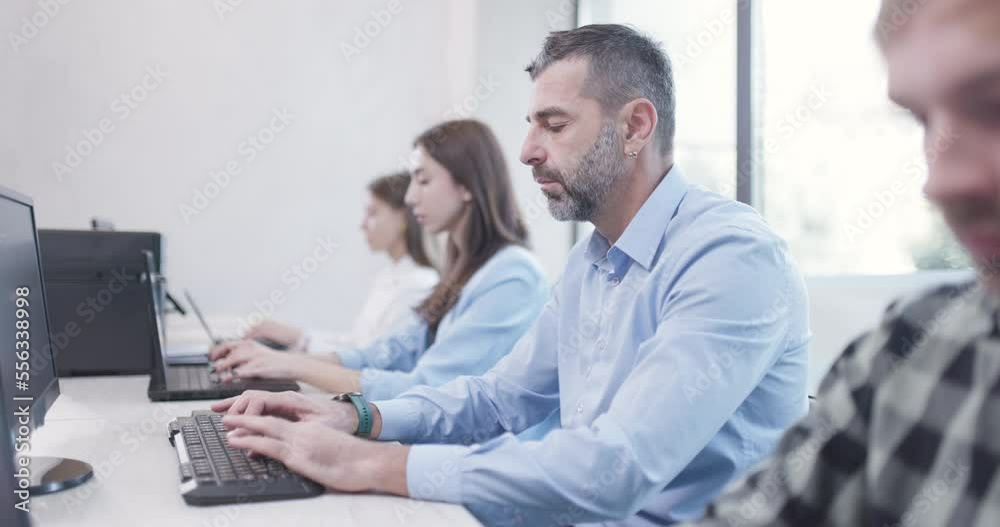 People sitting in a row in office working on laptop and desktop computers. Bussiness colleagues team. Shallow depth of field video. Forward camera movement. People sitting in a row in office working on laptop and desktop computers. Bussiness colleagues team. Shallow depth of field video. Forward camera movement.