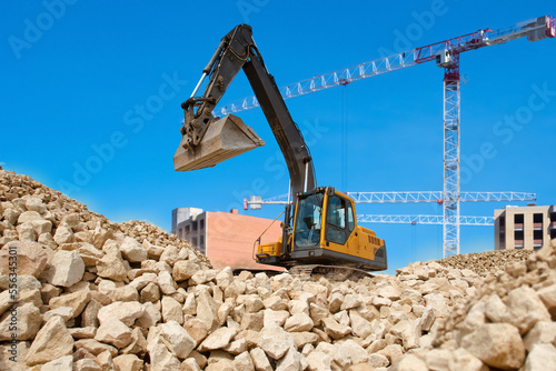 Excavator at construction site. Mountain of small stones with excavator on top. Preparation of site for construction of buildings. Crawler excavator on background sky. Special Construction machinery