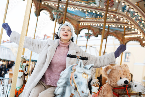 Beautiful and cheerful brunette woman in a fur coat rides on a carousel