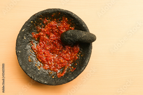Sambal or traditional chili sauce from Indonesia, freshly made using stone mortar and pestle. Flat lay or top view. Isolated in wooden background photo