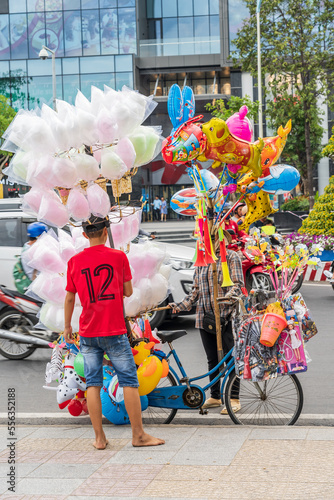 A street hawker selling brightly coloured toys and cotton candy from the back of a bicycle