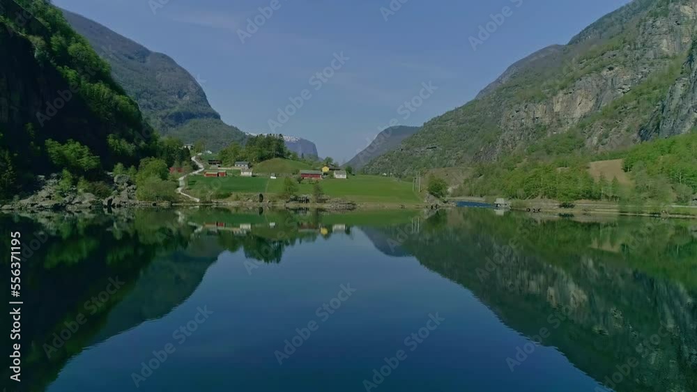 Aerial drone forward moving shot over a large lake surrounded by green mountain range with village houses at daytime.