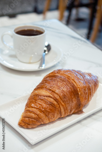 French croissant on white marble table with a cup of black coffee.