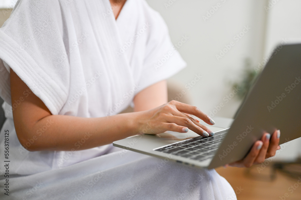 Naklejka premium cropped images, A female in bathrobe using laptop, typing on keyboard, work from home.