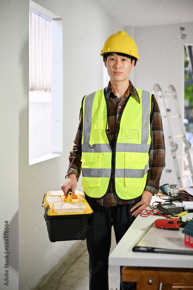 Professional Asian male construction worker in yellow hardhat and uniform holding a toolbox. Professional Asian male construction worker in yellow hardhat and uniform holding a toolbox.