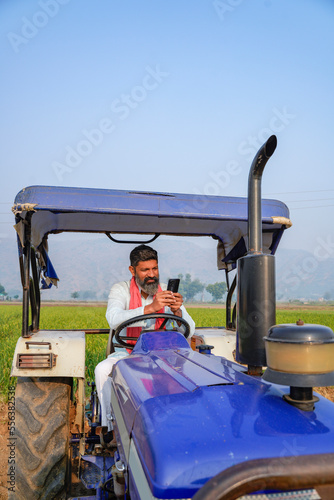 Indian farmer sitting tractor and using on smartphone.
