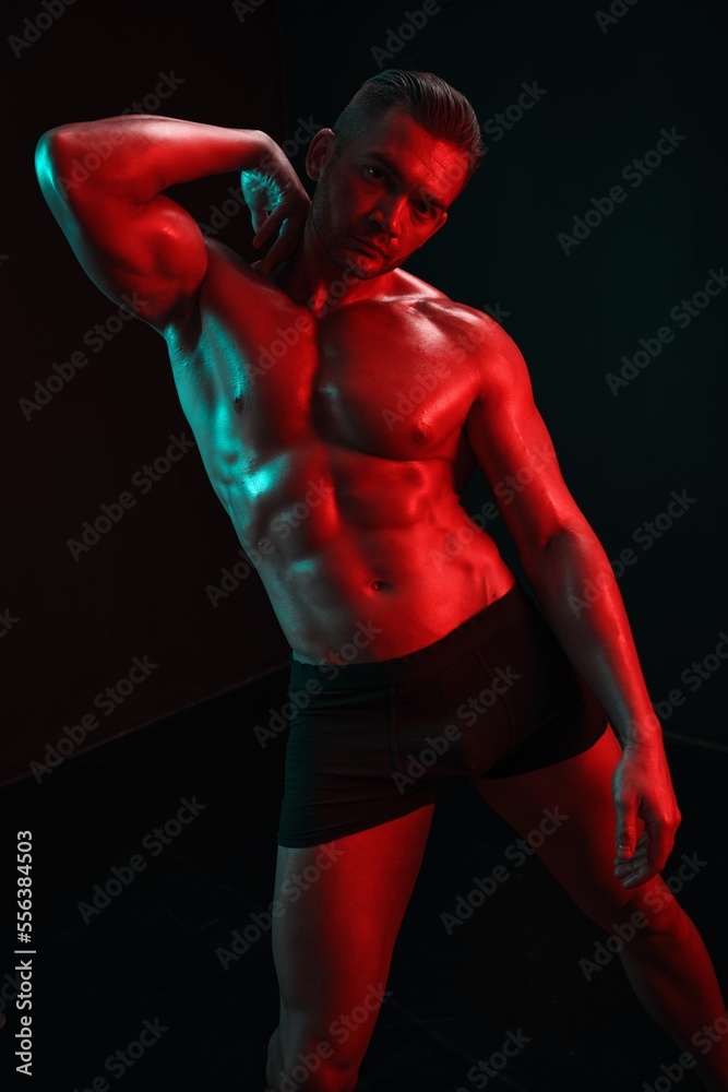 Man bodybuilder posing muscles with nude fitness torso, isolated on black background in neon light. Advertising, sports, active lifestyle, colored light, competition, challenge concept. Man bodybuilder posing muscles with nude fitness torso, isolated on black background in neon light. Advertising, sports, active lifestyle, colored light, competition, challenge concept.