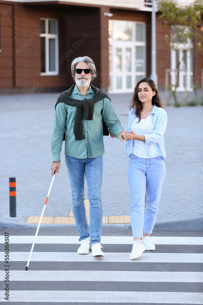 Young woman helping senior blind man to cross road in city Young woman helping senior blind man to cross road in city